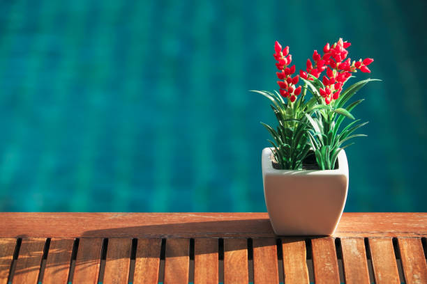 Red decoration artificial flower on wooden table with swimming pool background.