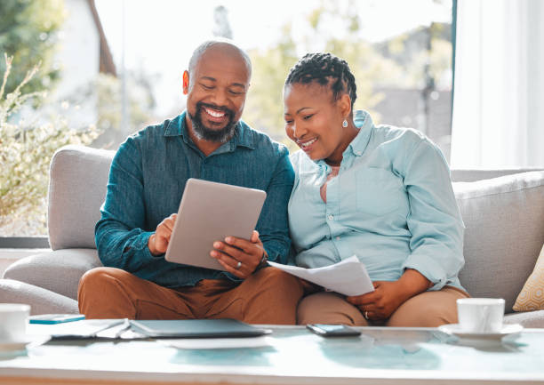 scatto di una coppia matura che guarda attraverso le loro bollette mentre usano un tablet digitale - home finances couple computer african ethnicity foto e immagini stock