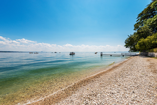 Beautiful empty beach on the coast of Lake Garda (Lago di Garda) near the small Garda town, Promontory or headland of San Vigilio (Punta San Vigilio), Verona province, Veneto, Italy, Europe. On the horizon, the coast of Lombardy on the right.