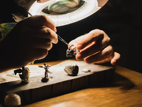 human hands painting under the lamp with light and magnifying glass plastic minifigures for board games , modern hobby of game collector