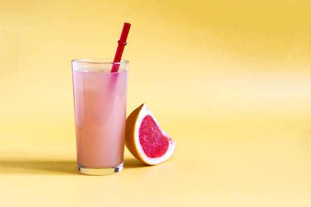 istock Grapefruit juice and a slice of grapefruit on a yellow kopi space background. Grapefruit juice in a glass glass with a red tube on a yellow background in natural light 1368552384