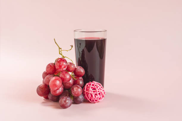 A vine with red berries and a transparent glass with grape juice and red decor on a light background.