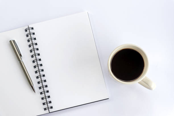 istock Blank spiral notebook with pen and a cup of morning coffee on white table background. 1368553843