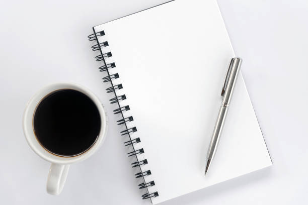 istock Blank spiral notebook with pen and a cup of morning coffee on white table background. 1368553885