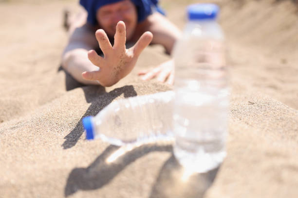 목마른 남자가 물 한 병을 위해 도달하는 모래에 누워 있습니다. - thirsty desert men reaching 뉴스 사진 이미지