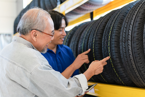 Asian senior customer man choosing wheel tires with man salesman at auto store shop and car repair service