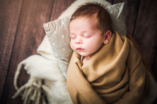 Newborn baby photographed on a wooden floor in a basket with blankets.