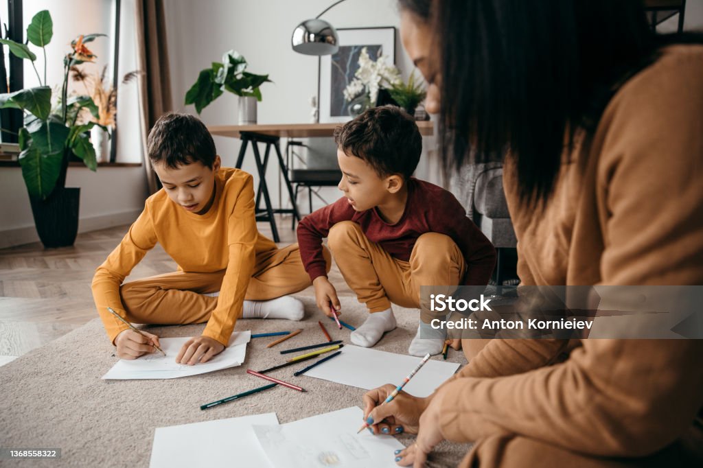 Happy african american mom teaching her sons to draw with pencils. Mother's day concept. Happy african american mom teaching her sons to draw with pencils. Mother's day concept. . High quality photo Mother Stock Photo