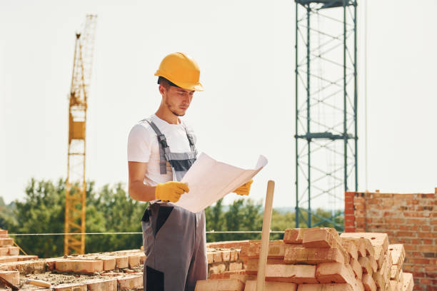 istock Holding document. Young construction worker in uniform is busy at the unfinished building 1368559106