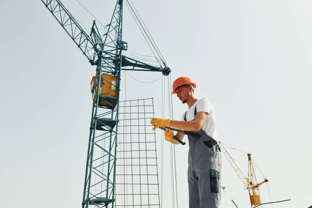 istock Crane is at background. Young construction worker in uniform is busy at the unfinished building 1368559208