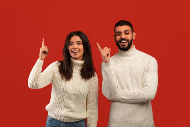 istock Middle eastern couple pointing fingers up, having great idea and smiling to camera, standing over red studio background 1368559755