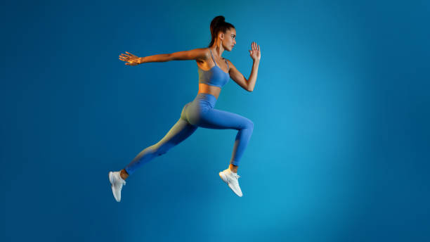 istock Determined Young Sportswoman Jumping Posing In Mid-Air On Blue Background 1368562475