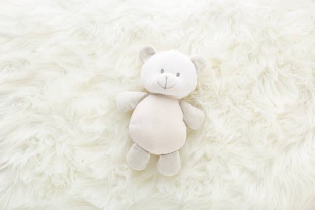 istock Smiling baby teddy bear on white fluffy fur blanket background. Closeup. Top down view. 1368562586