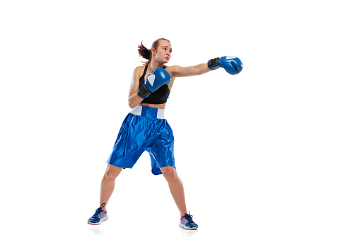 Punching. Dynamic portrait of young girl, professional boxer practicing in boxing gloves isolated on white studio background. Sport, competition, show, power, action concept.