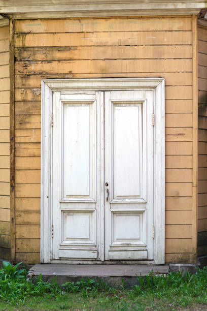 une vieille porte blanche à double vantail dans une vieille maison en bois. la façade est gainée de planches jaunes. les planches sont fortement altérées et vieillies - weatherd photos et images de collection