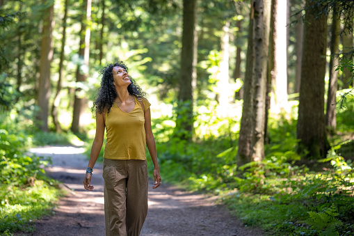Smiling mature woman looking upwards while walking on dirt track passing through forest.