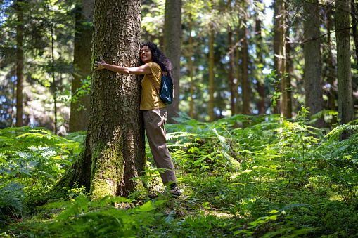 Side view of a smiling mature woman with eyes closed embracing a tree in forest.