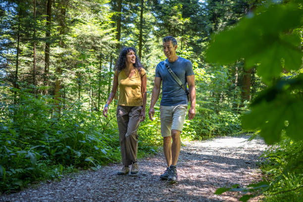 Smiling mature couple talking with each other while walking on dirt track passing through forest.