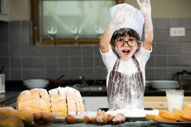 asiatischer kleiner junge in schürze bereitet das backen des teigs in der küche zu hause vor - little cakes stock-fotos und bilder