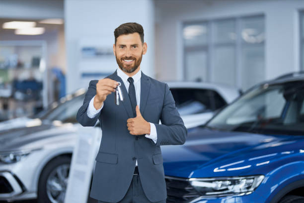 Businessman showing thumb up and holding keys from new car stock photo