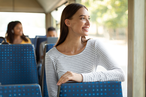 Road Trip. Portrait on smiling casual young woman taking bus, sitting on seat and looking out of window, excited female passenger daydreaming, enjoying journey travel or ride on city tram