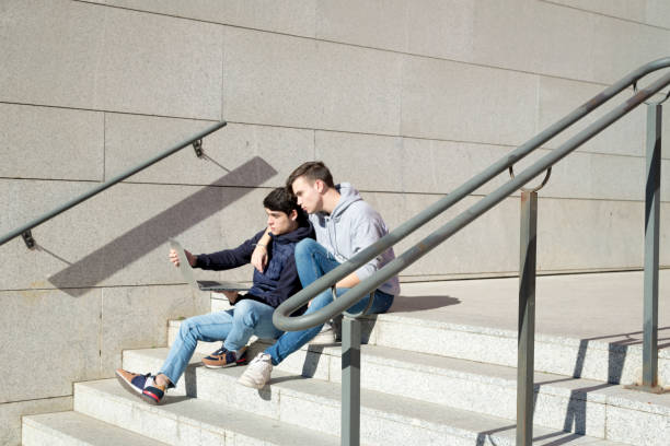 istock two gay student boys sitting on a staircase using a laptop computer 1368566432