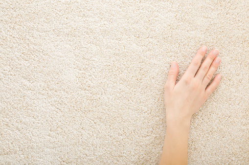 Young adult woman hand touching beige new fluffy home carpet. Closeup. Checking softness. Empty place for text. Top down view.