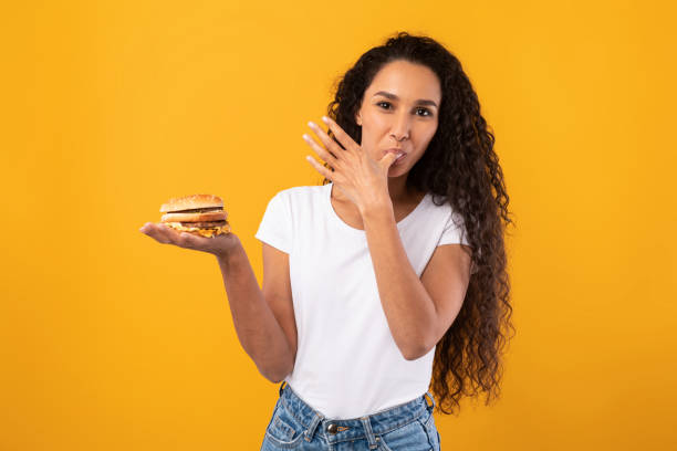 happy latin lady holding burger lizanie palca w studio - finger licking zdjęcia i obrazy z banku zdjęć