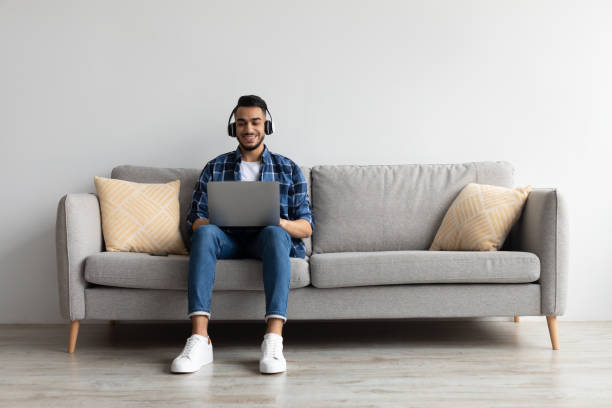 istock Smiling Arab man in headphones using pc at home 1368568584