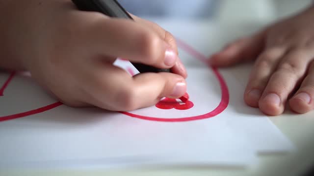 Child draws hearts on paper with pink markers. Close-up. Children's creativity. St. Valentines day