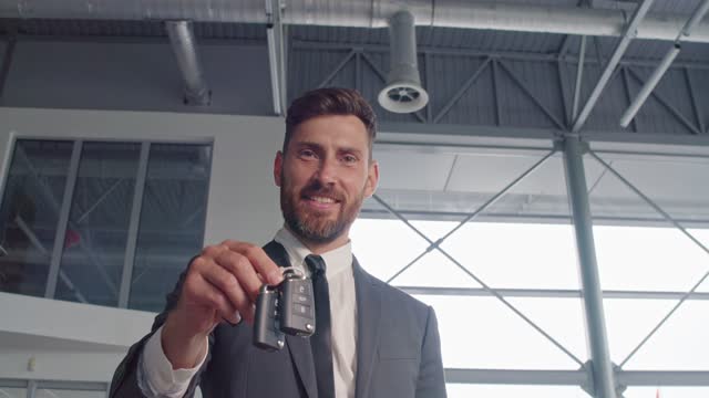 Man in stylish suit holding keys from new auto at salon