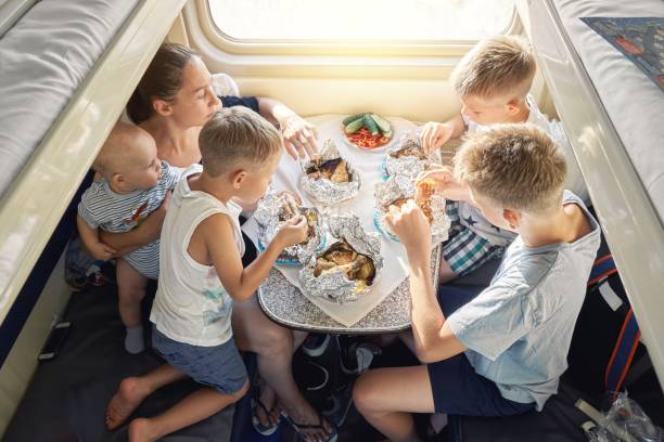Family having lunch at table in train car in morning Family of mother holding baby and sons sitting at table and having lunch in train car with bunk beds against bright sunlight boys bowl haircut stock pictures, royalty-free photos & images