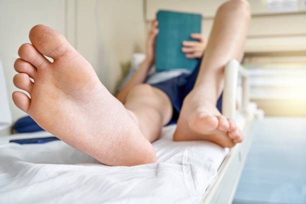 istock Bare feet of boy lying on bed and playing games on tablet 1368572680