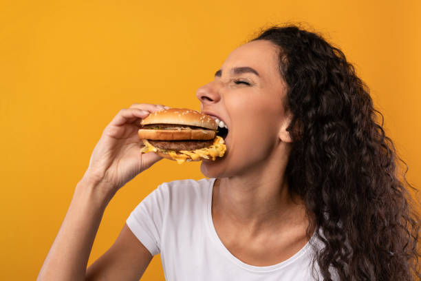 lustige hungrige latin lady mit burger beißsandwich im studio - verlangen verhalten und emotionen stock-fotos und bilder