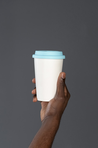 African man hand with cardboard cup or disposable cup for coffee or tea. White disposable cup with blue plastic lead in mans hand. Disposable dishes concept. Copy space.