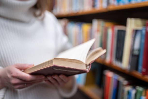 istock Young woman holding old book in the library 1368584445
