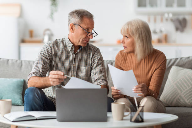 istock Senior Couple Holding Papers Reading Documents Sitting At Laptop Indoor 1368585636