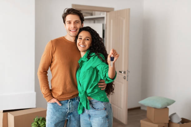 Happy couple showing keys from flat on moving day House Ownership. Portrait Of Happy Young Couple Holding Showing Key Standing In New Flat, Cheerful Guy Embracing Lady Posing After Moving In Own Apartment. Insurance, Real Estate, Mortgage Concept young couple stock pictures, royalty-free photos & images