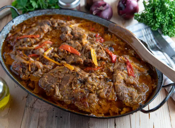 Spicy sliced pork neck cooked with onions, garlic and bell peppers. Served in a rustic roasting pan on wooden table background. Savory meat dish. Ready to eat