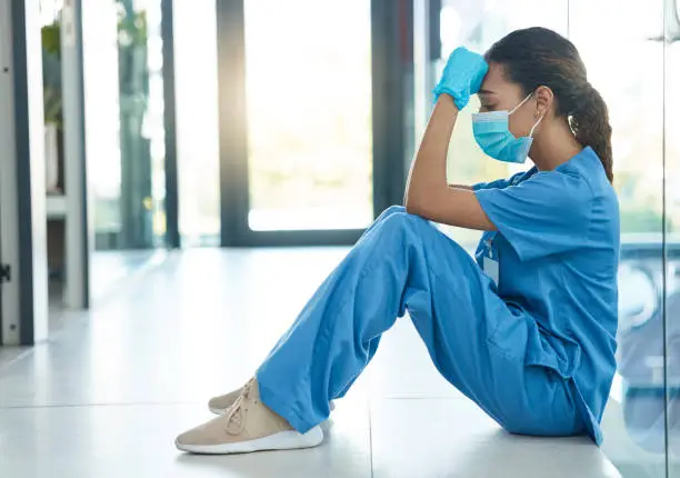 Photo of Shot of a female nurse looking stressed while sitting in a hospital