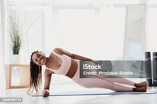 istock Beautiful young black woman standing in side plank on yoga mat at home, free space 1368589733