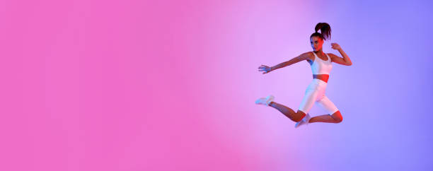 istock Athletic Lady Jumping Posing In Mid-Air Exercising Over Neon Background 1368589837