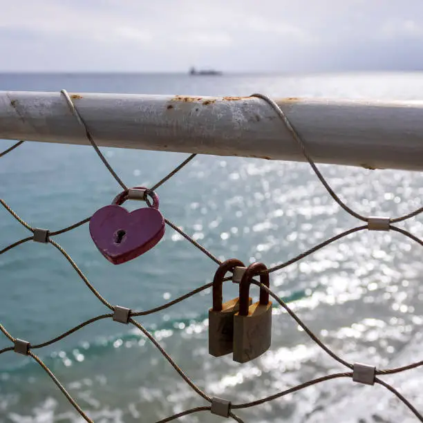 Love locks hanging on metal bridge fence in front of the sea