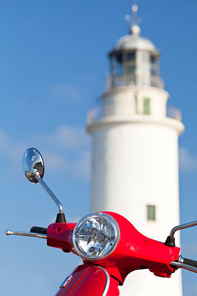 Detail of a red scooter and lighthouse on the background. Formentera island. Spain.