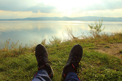 A man lies on the grass and looks at the lake and mountains. Landscape. Background.