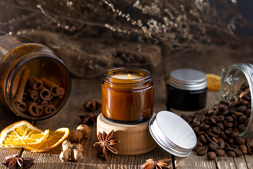Scented candle in a glass jar. Coffee aroma. Star anise, cinnamon sticks, dried orange. Still life. Coffee beans. Brown jars with candles. Aromatherapy