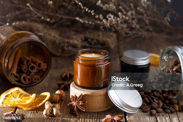 Scented Candle In A Glass Jar Coffee Aroma Star Anise Cinnamon Sticks Dried Orange Still Life Coffee Beans Brown Jars With Candles Aromatherapy Stock Photo - Download Image Now