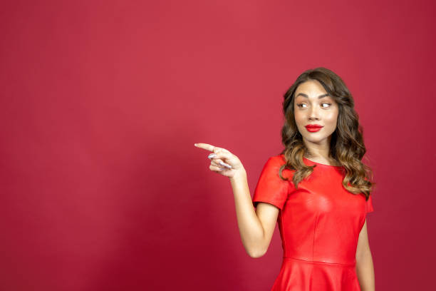 istock Woman mysteriously smiles and points with her finger on a red background 1368594980