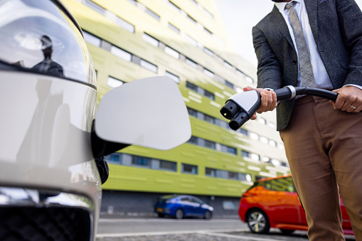 A low angle of an unrecognizable man leaning down towards his car and charging at a convenient public electric vehicle charging station in Newcastle upon Tyne in the North East of England.