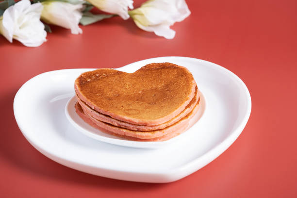 Creative breakfast for Valentine's Day. Heart shaped pancakes on a red background with flowers. Valentine's day background. Top view.